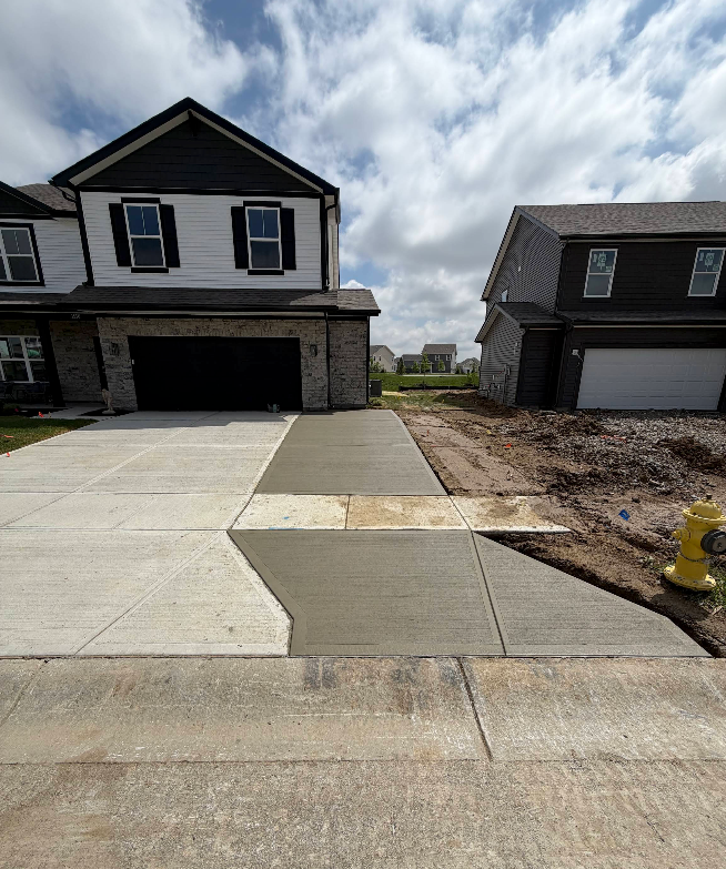 New suburban houses with driveways and unfinished dirt lot under cloudy sky