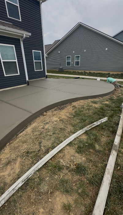 Curved concrete walkway beside a dark blue house and gray garage, with grass and a wooden border.