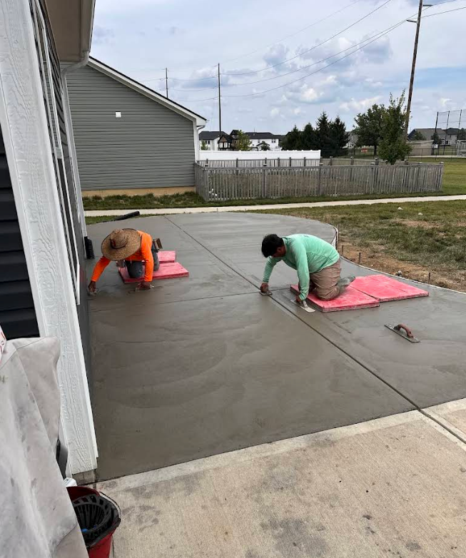 Two workers smoothing fresh concrete on a driveway beside a house