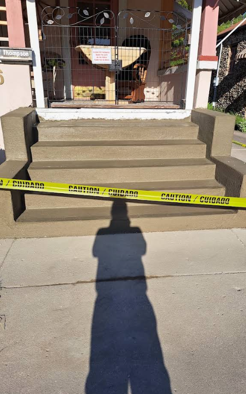 Yellow caution tape blocking storefront steps and entrance behind a shadow on the sidewalk