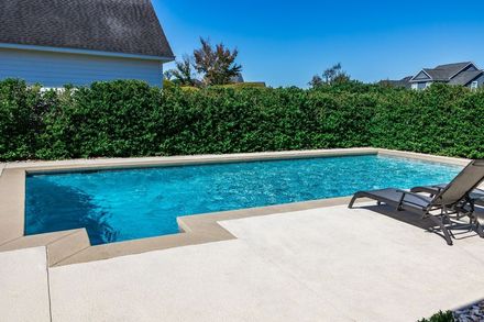 Backyard swimming pool with blue water, white patio, hedge, and lounge chairs