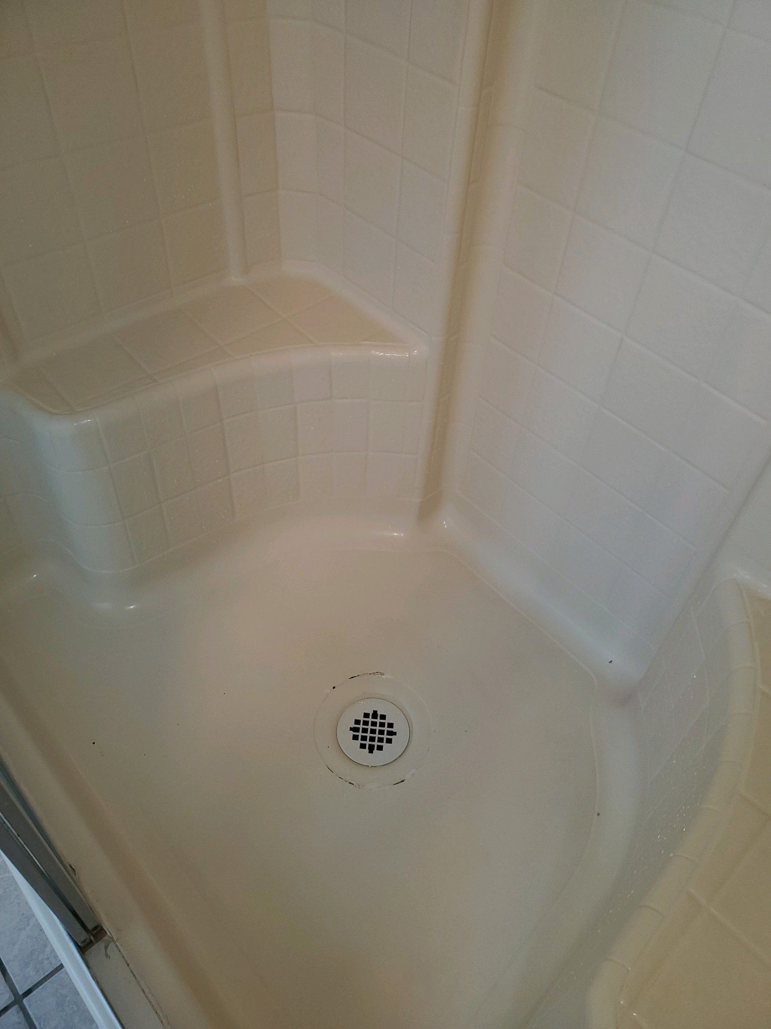 Beige corner shower with built-in seat and drain.