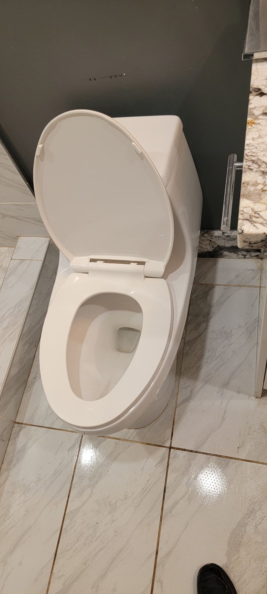 White toilet with the lid up, in a tiled bathroom.