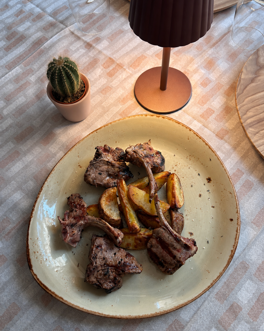 Un piatto di carne alla griglia e patate arrosto su un tavolo accanto a un piccolo cactus e una lampada.