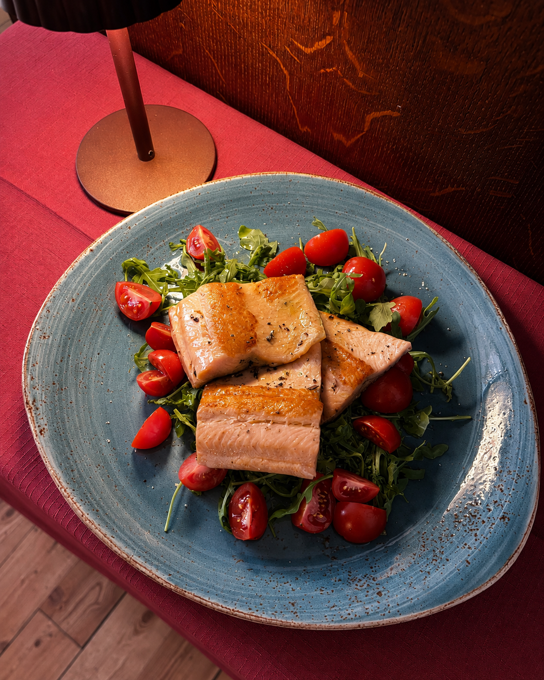 Tramezzino grigliato su un piatto blu con fragole e verdure su una tovaglia rossa.
