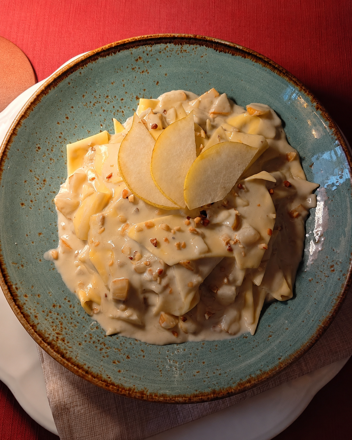 Dessert cremoso guarnito con fettine di pera e noci su un piatto blu.