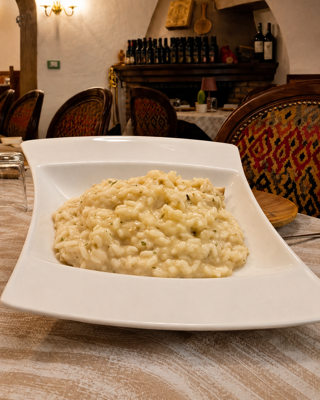 Risotto cremoso servito su un piatto quadrato bianco nell'accogliente sala da pranzo di un ristorante.
