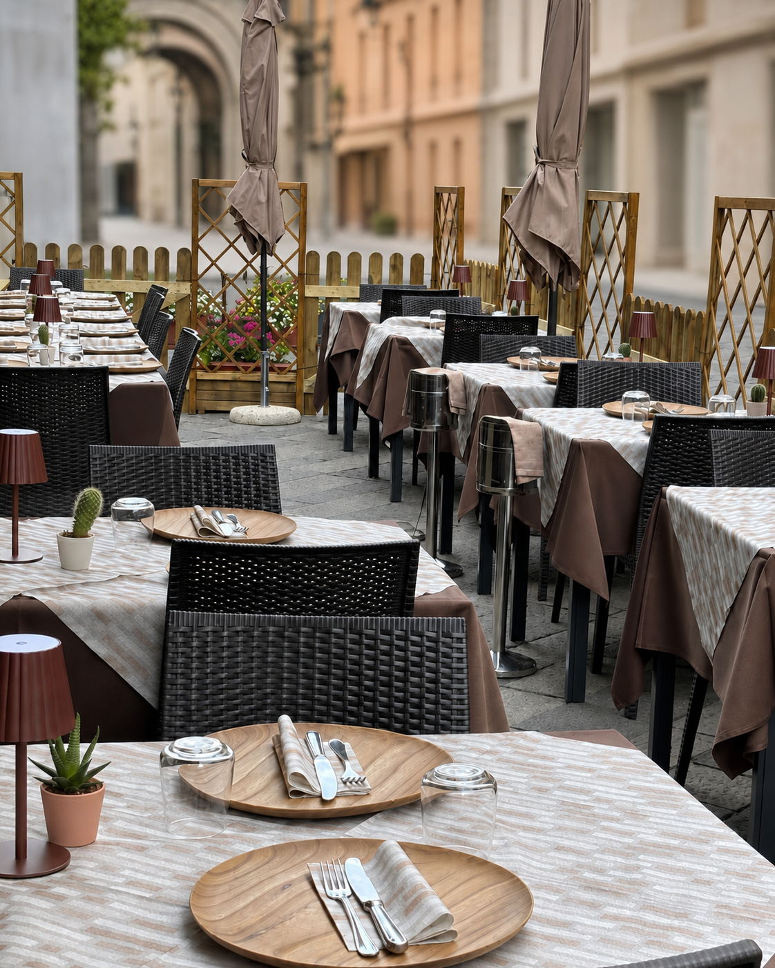 Tavolini da caffè all'aperto e sedie di vimini disposti lungo una strada tranquilla, apparecchiati con piatti e posate.