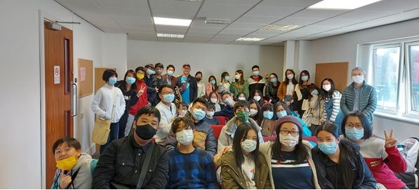 A group of people wearing face masks are sitting in a room.