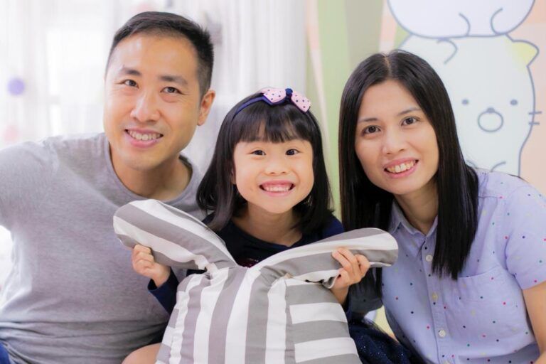 A family posing for a picture with a little girl holding a pillow.