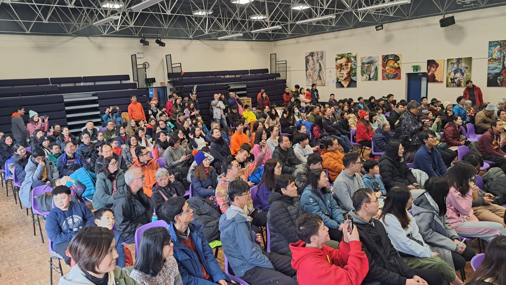 A large group of people are sitting in a gym.