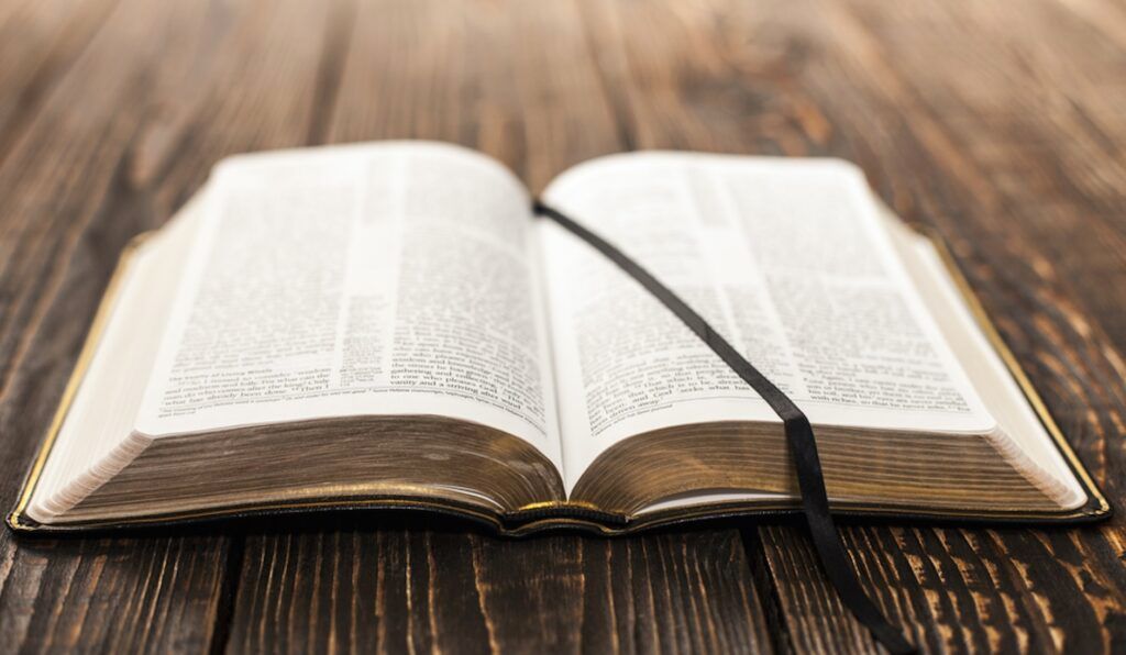 An open bible with a black ribbon on a wooden table.