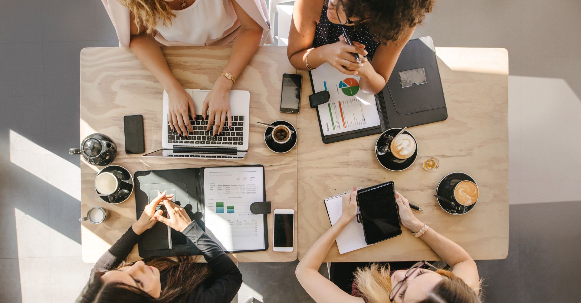 A group of women are sitting at a table with a laptop and a tablet.