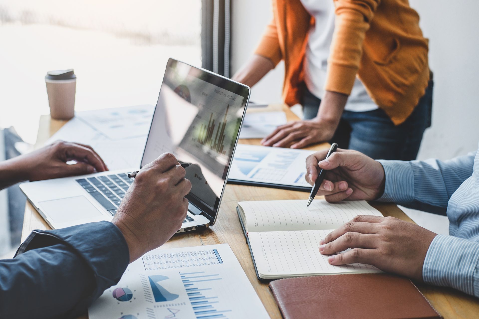 Business meeting: people reviewing data on a laptop, documents, and a notebook in a modern office.