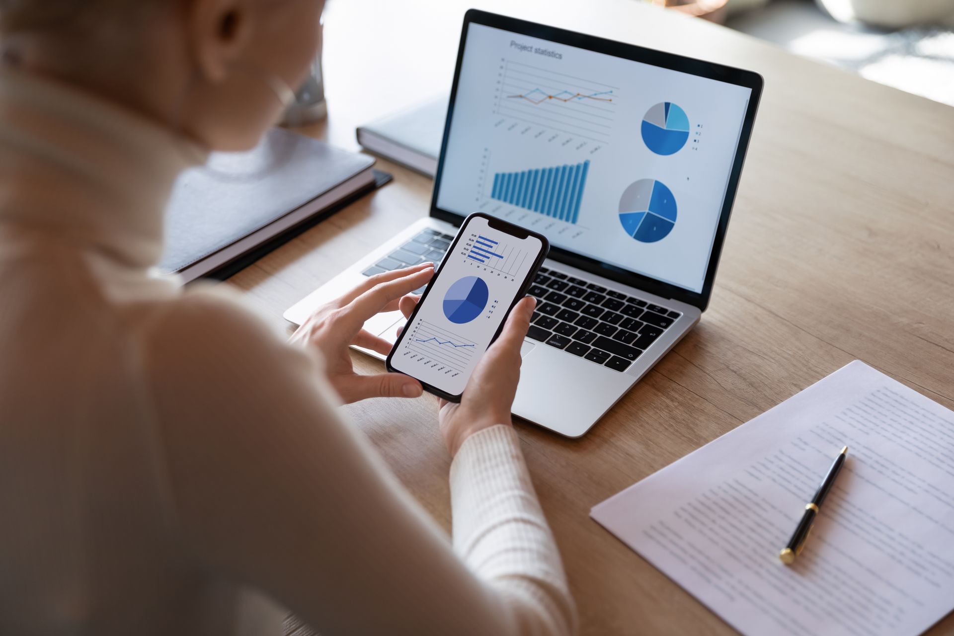 Person viewing data charts on laptop and phone at a desk.
