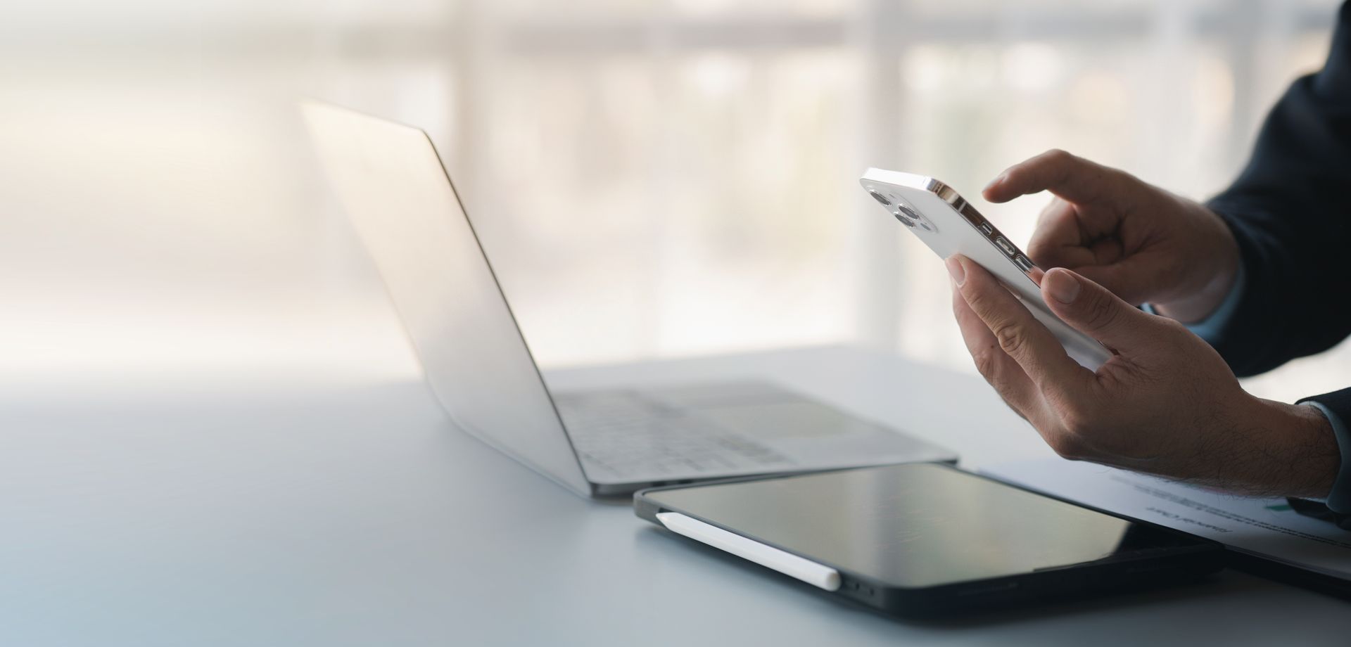 A person is using a cell phone in front of a laptop computer.