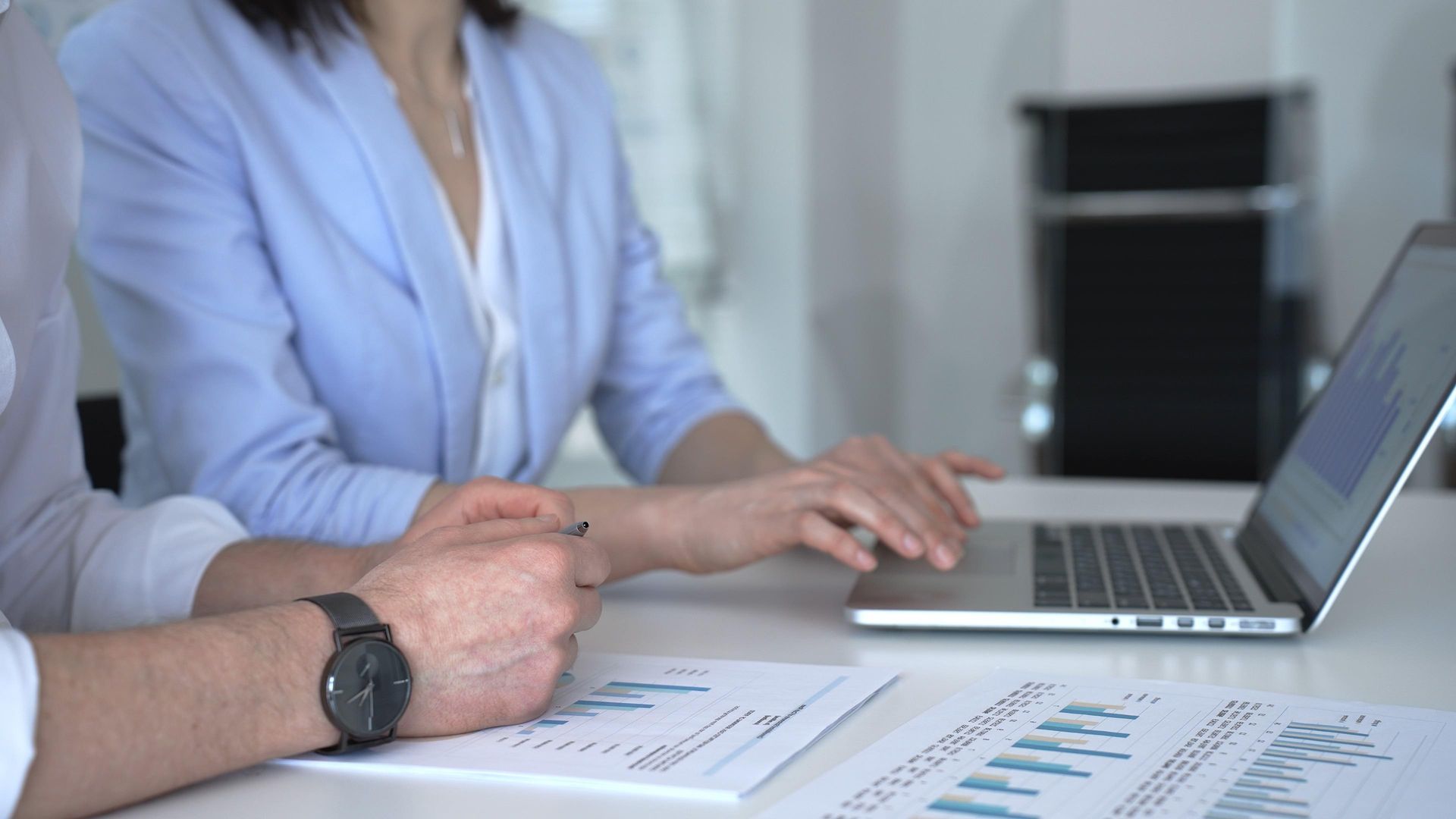Two colleagues reviewing performance reports on a laptop and printed documents