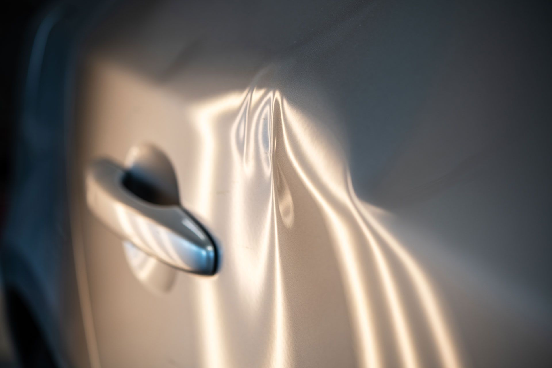 Dented car door with distorted reflections of light and a door handle.