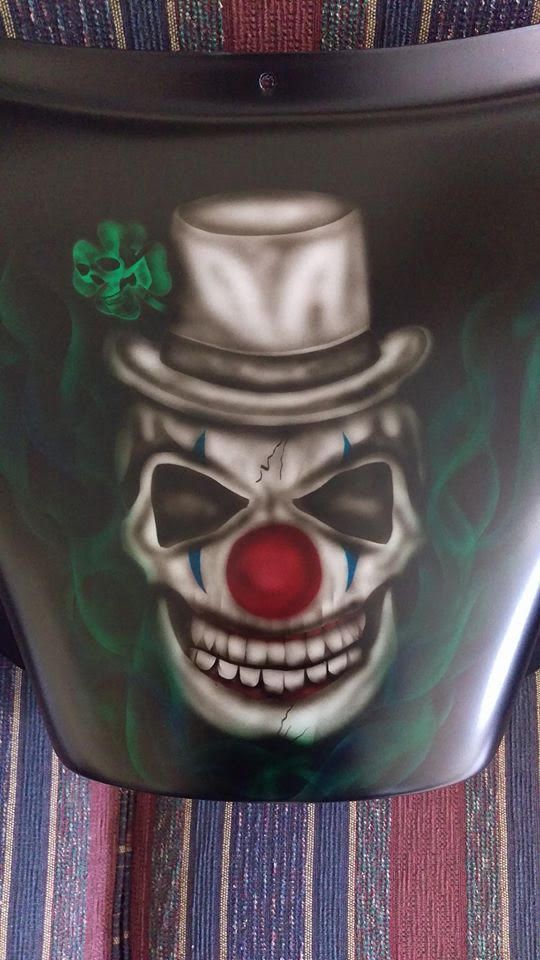 Scary clown skull wearing a hat, surrounded by green smoke, on black surface.