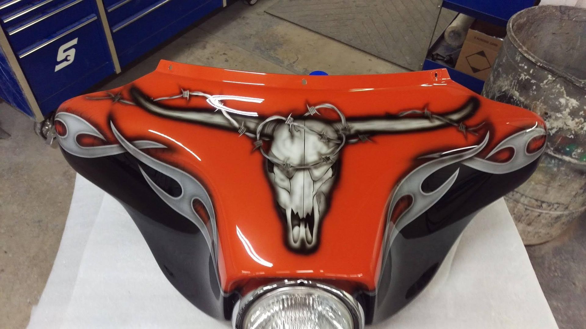 Motorcycle fairing with a skull design on orange and black paint, with silver flames.