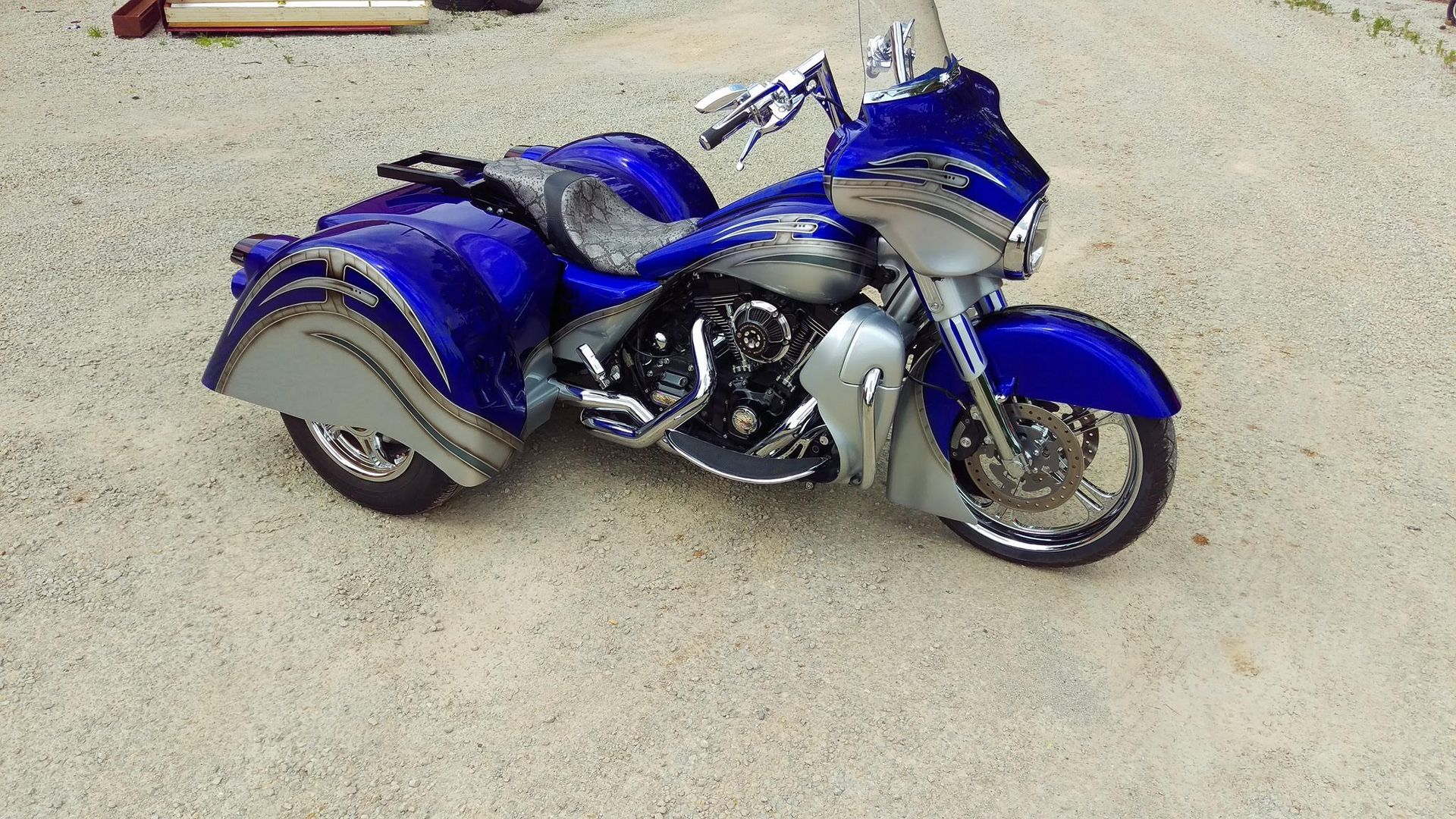Blue and silver custom trike motorcycle parked on gravel.