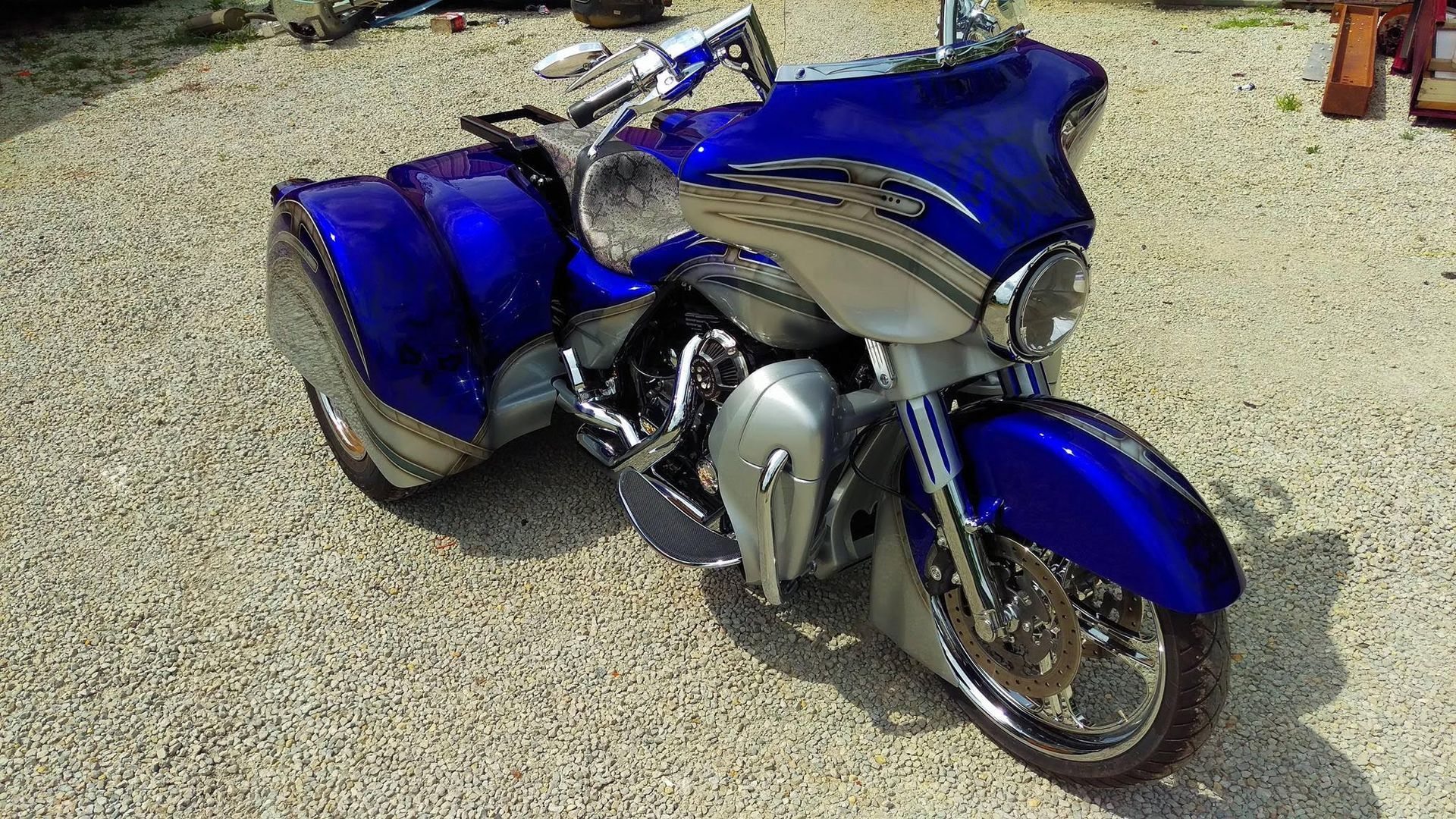 Blue and silver custom trike motorcycle parked on gravel.