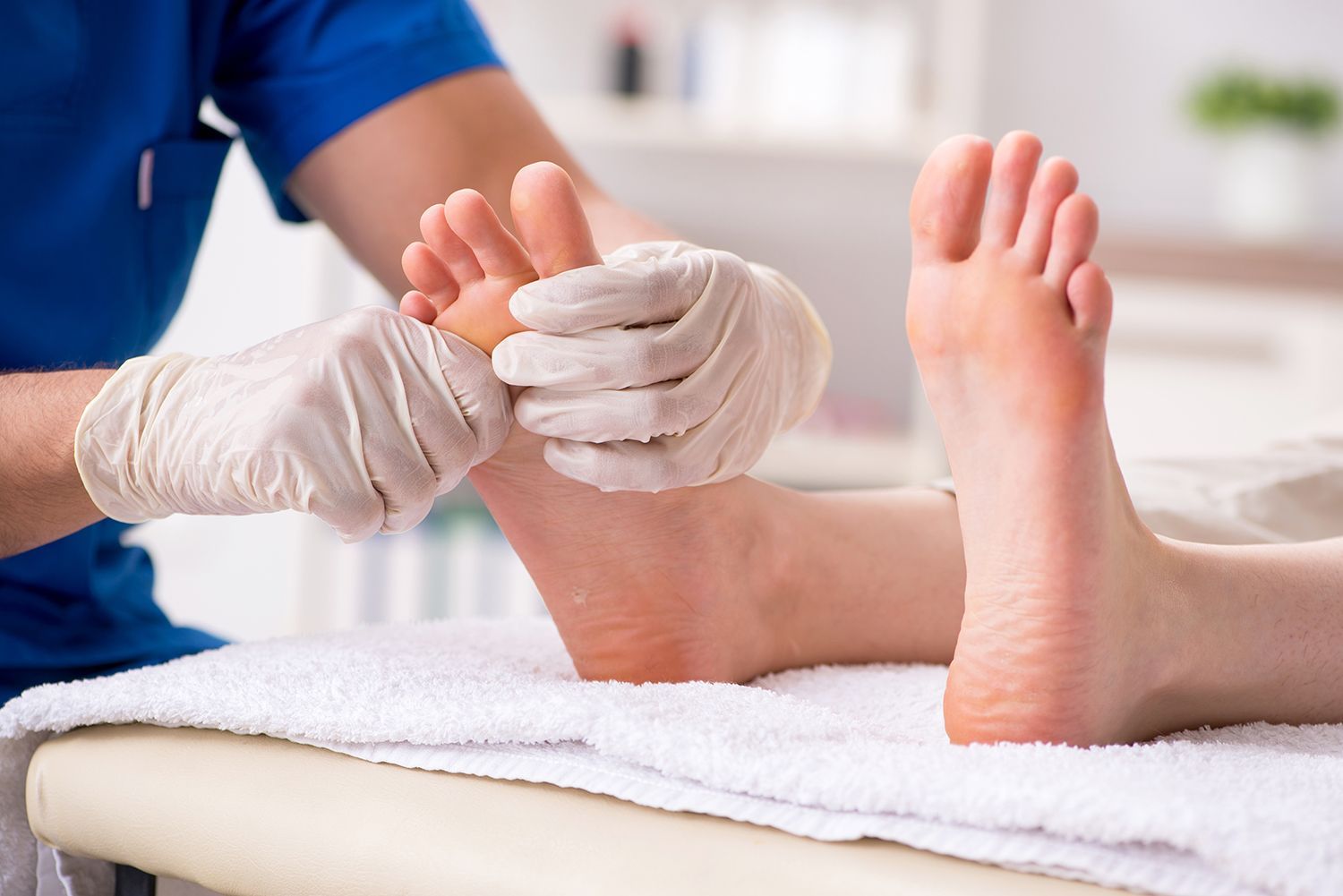A medical professional examining a patient's feet. Podiatrist treating a patient’s foot with a towel on a treatment table