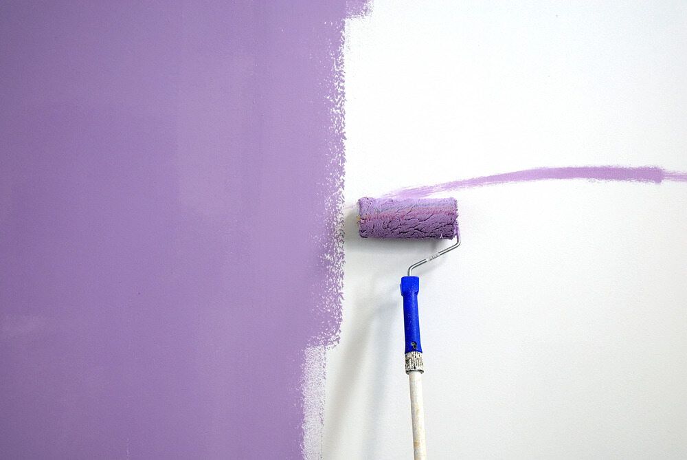 A Purple Paint Roller is Being Used to Paint a White Wall — Supremacy Painting Co In Edmonton, QLD