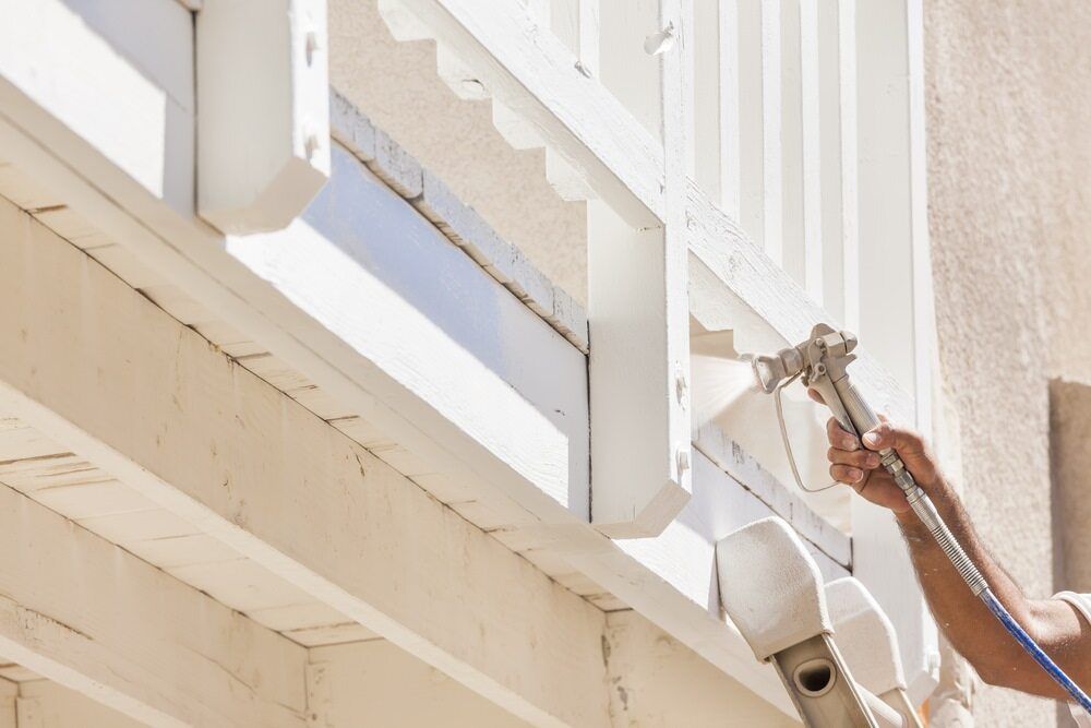 Person Using a Spray Gun to Paint the Exterior of a White Wooden Structure — Supremacy Painting Co In Redlynch, QLD