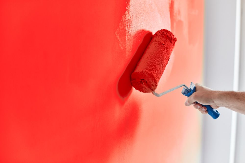 A Person is Painting a Red Wall With a Paint Roller — Supremacy Painting Co In White Rock, QLD