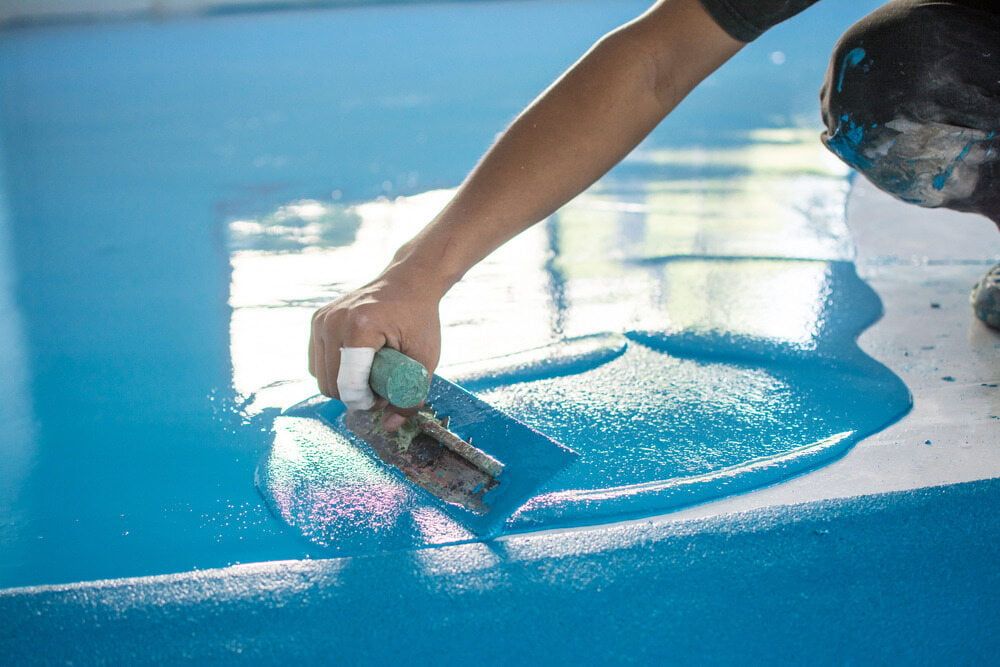 A Person is Painting a Blue Floor With a Trowel — Supremacy Painting Co In Edmonton, QLD