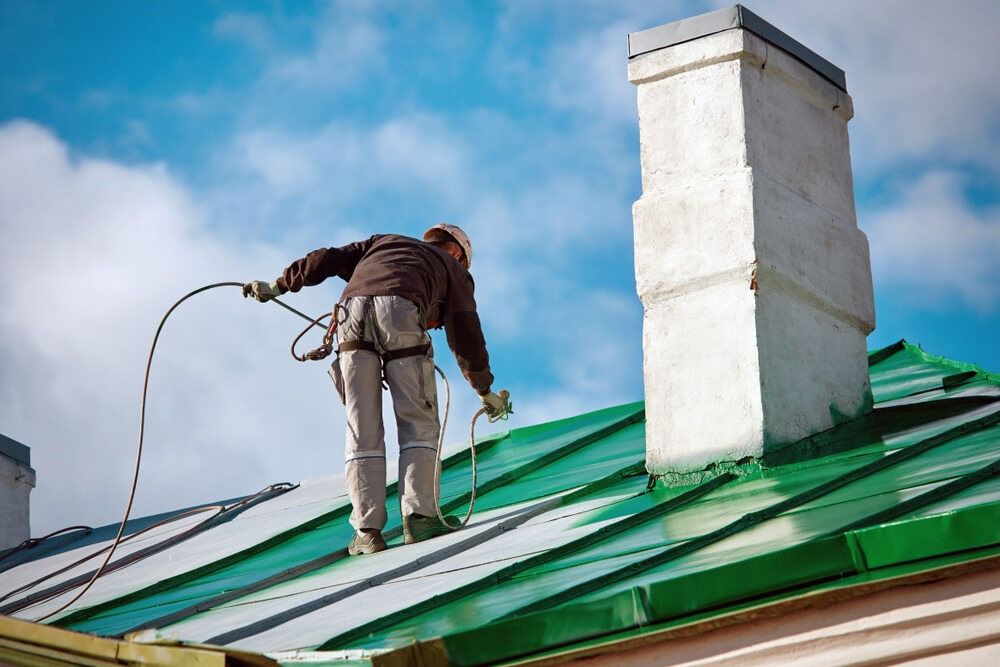 A Man is Painting the Roof of a Building With a Sprayer — Supremacy Painting Co In White Rock, QLD
