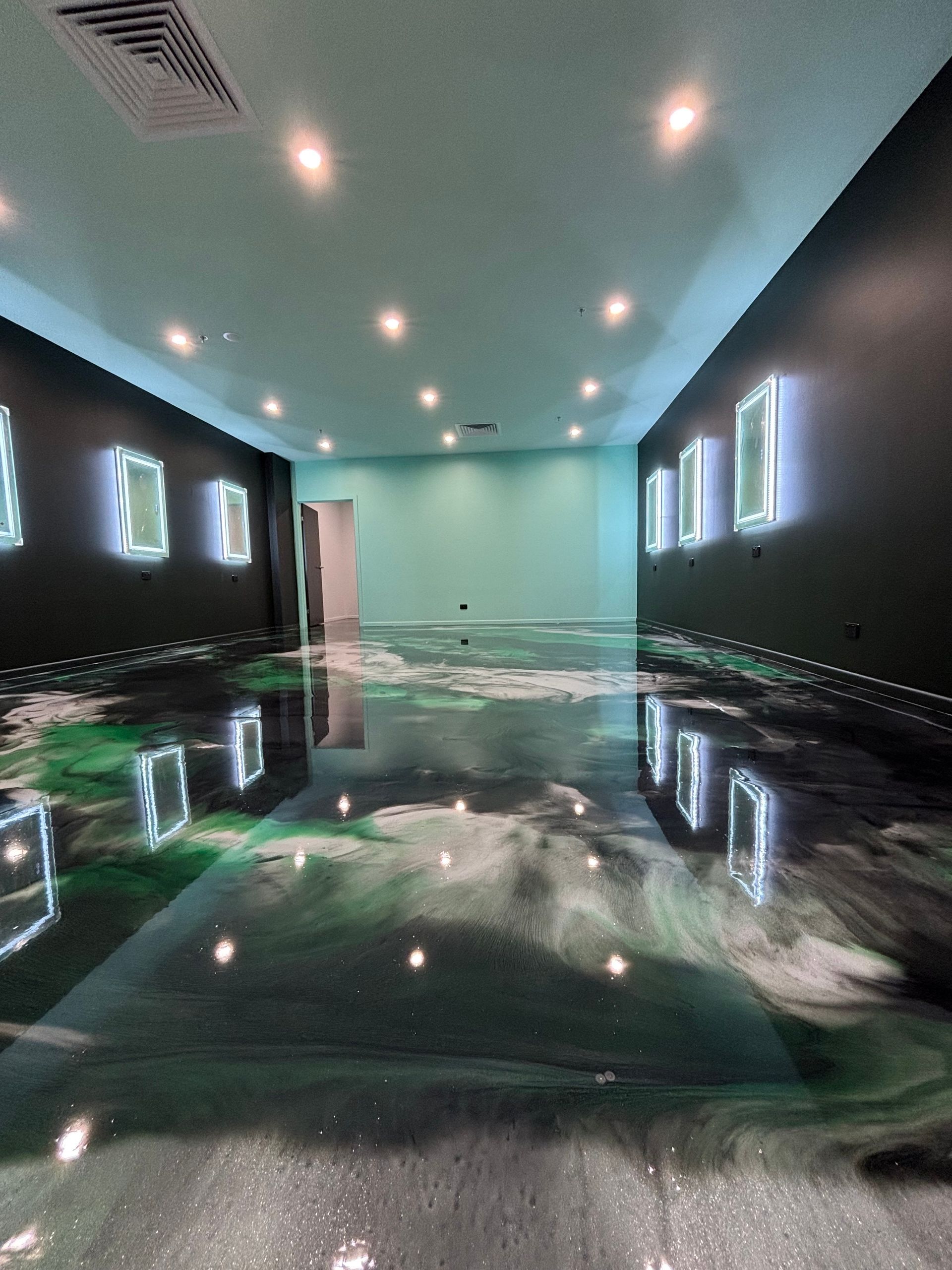 Room with reflective epoxy floor featuring green, black, and white swirls. Black and teal walls, illuminated frames — Supremacy Painting Co In White Rock, QLD
