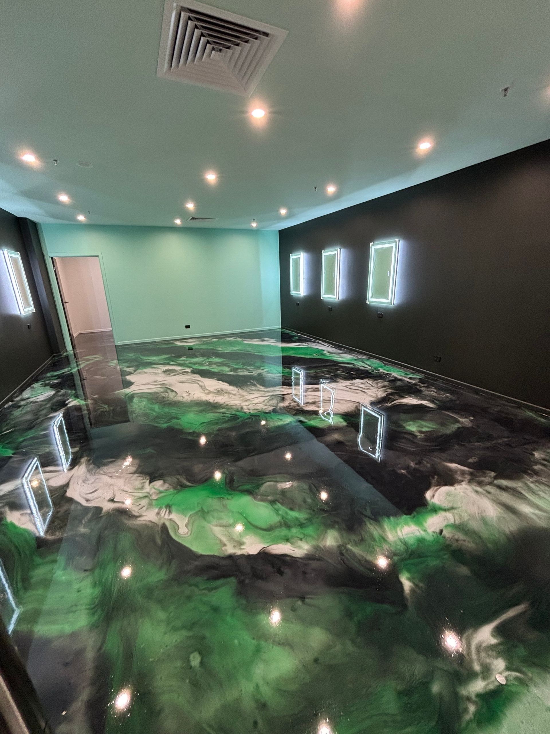 Room with reflective epoxy floor featuring green, black, and white swirls. Black and teal walls, illuminated frames — Supremacy Painting Co In White Rock, QLD