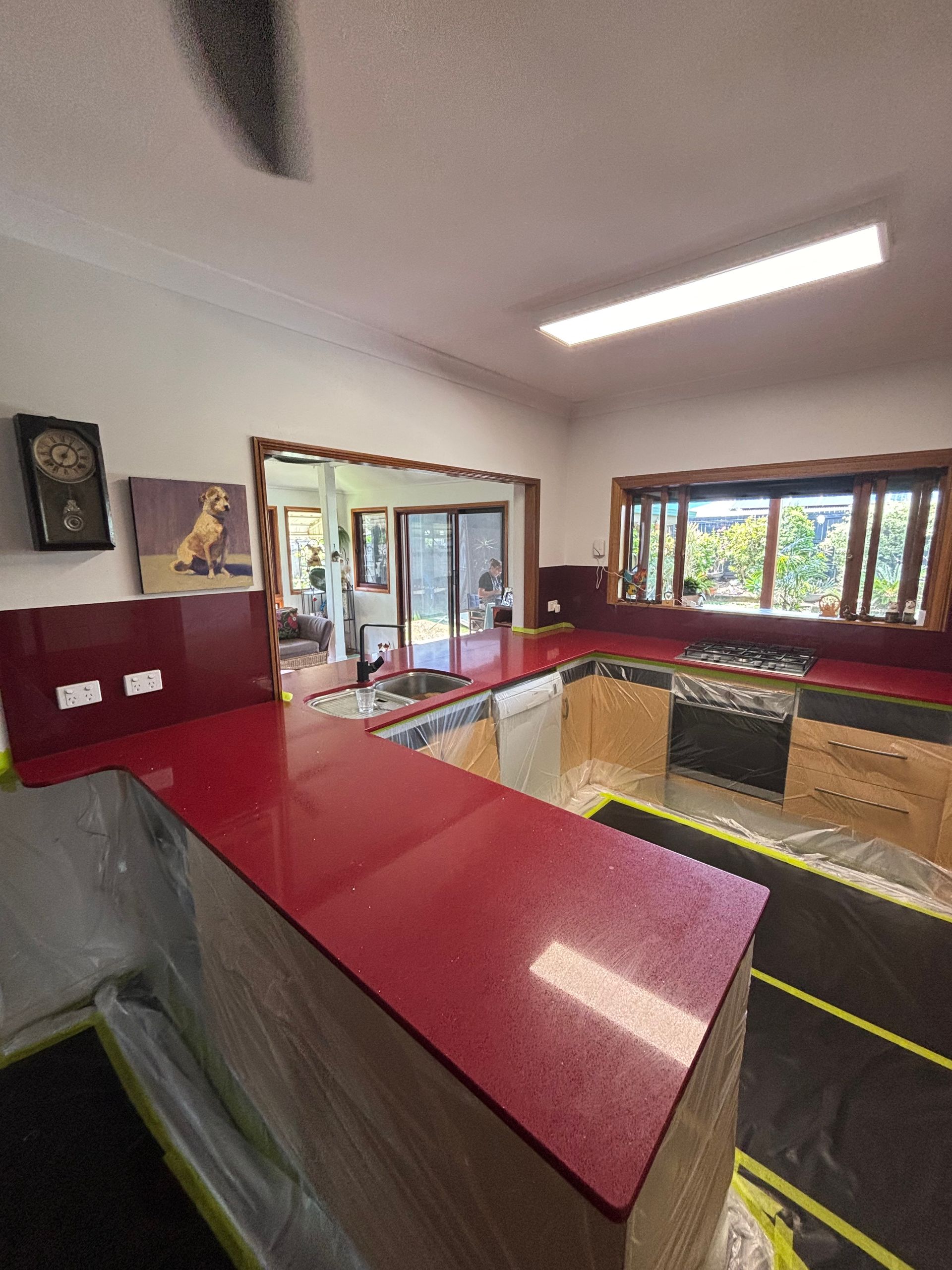 Red countertops in a bright kitchen with a window, sink, and maroon wall accents. — Supremacy Painting Co In White Rock, QLD