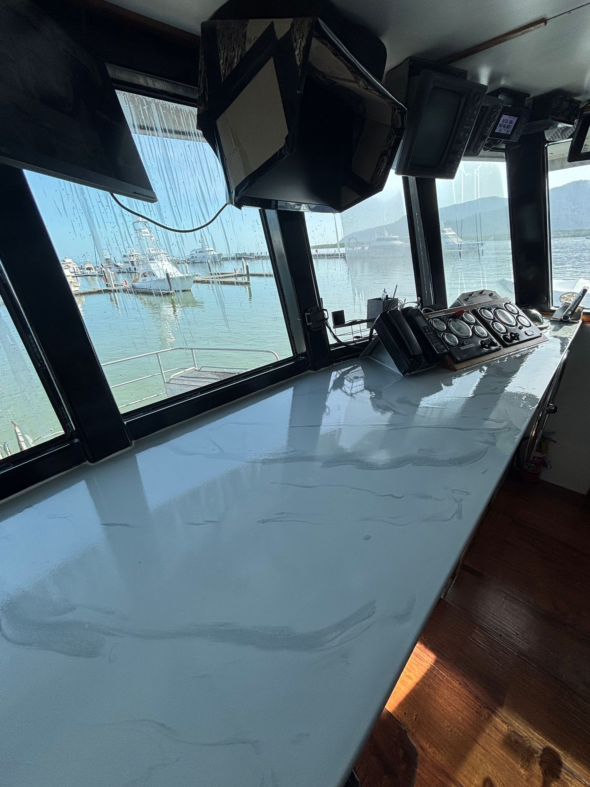 Long white table by windows overlooking water, with hanging speakers and stools in a modern room — Supremacy Painting Co In White Rock, QLD