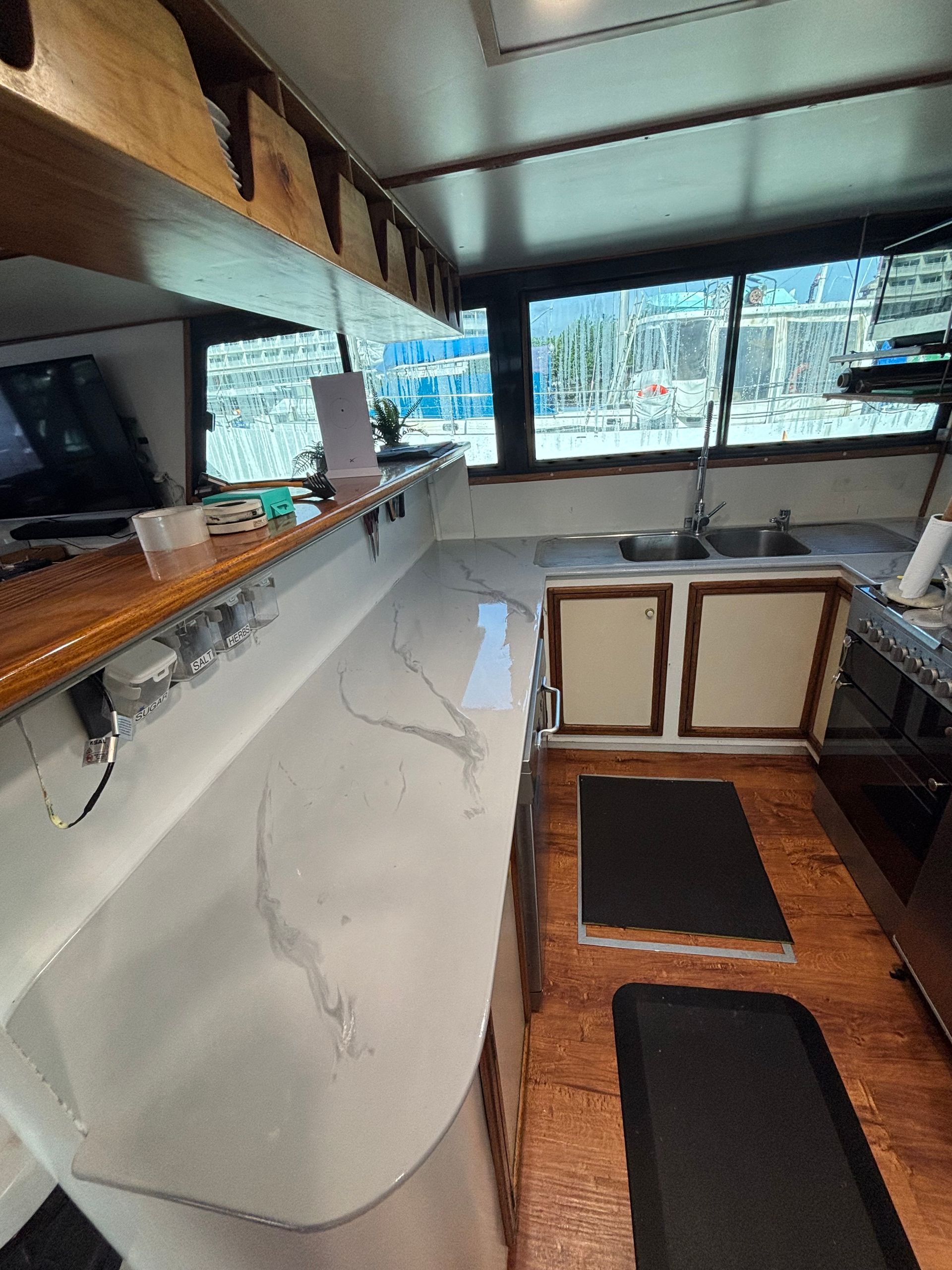 Compact boat cabin with white counter, wooden cabinets, bench seating, and windows overlooking water. — Supremacy Painting Co In White Rock, QLD