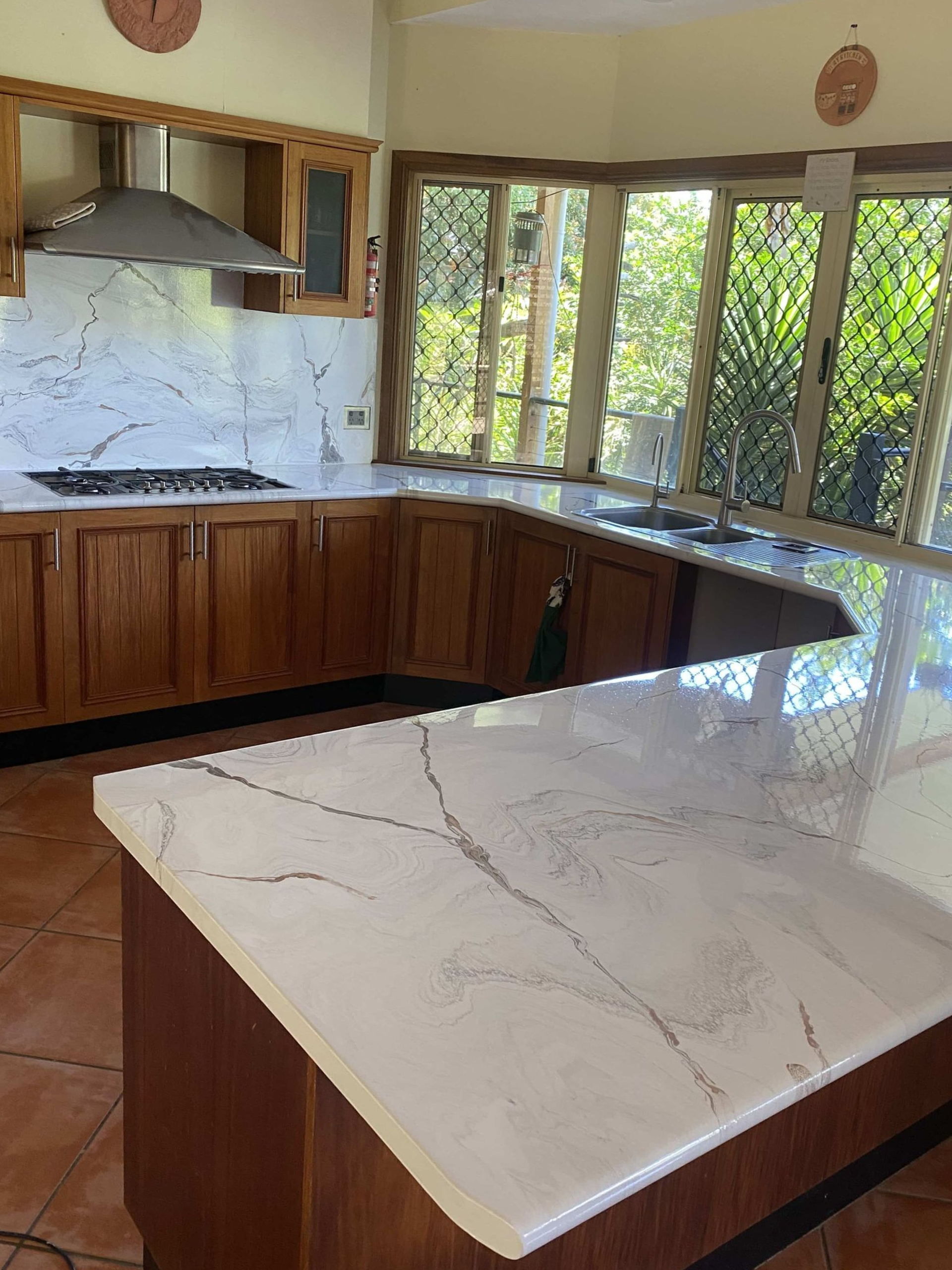 Modern kitchen with white marble island, wood cabinets, and large corner windows overlooking greenery — Supremacy Painting Co In White Rock, QLD