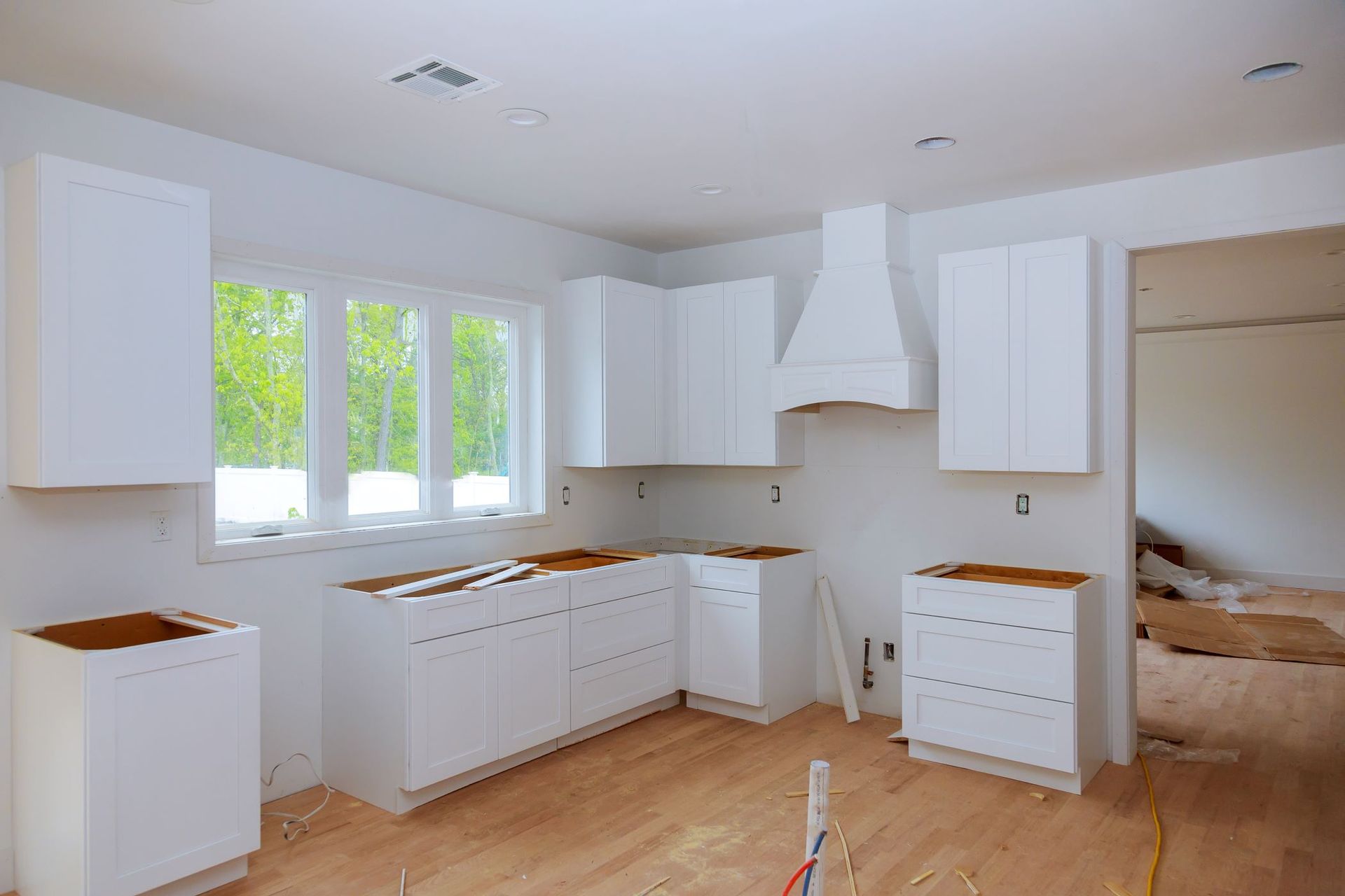 A kitchen under construction with white cabinets and hardwood floors.