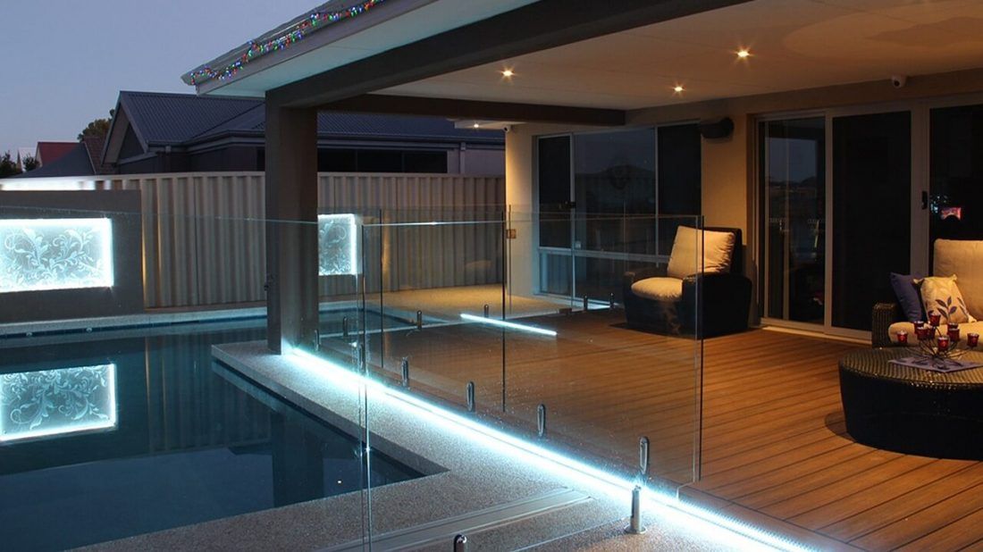 A swimming pool is surrounded by a glass fence and a wooden deck.