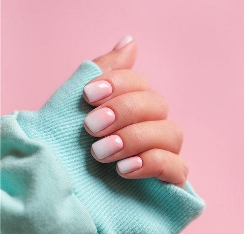 Eine Nahaufnahme einer Frauenhand mit rosa Nägeln auf einem rosa Hintergrund.