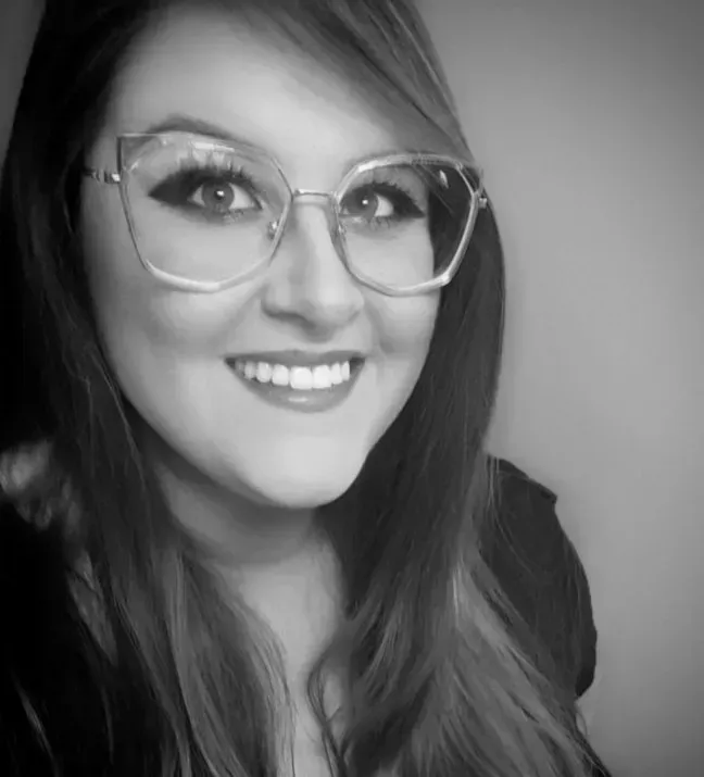 A woman wearing glasses is smiling in a black and white photo.