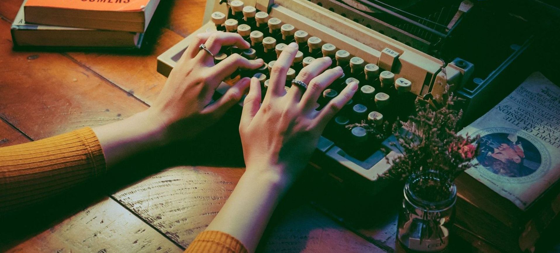 A person is typing on an old typewriter on a wooden table.