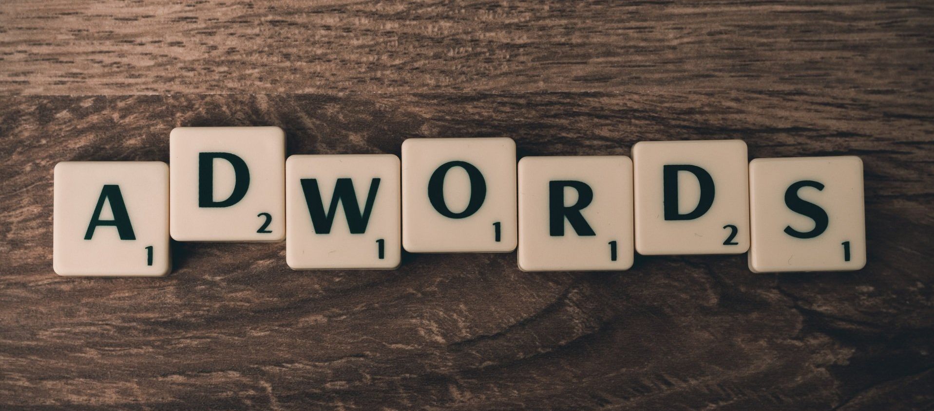 The word adwords is written in scrabble tiles on a wooden table.