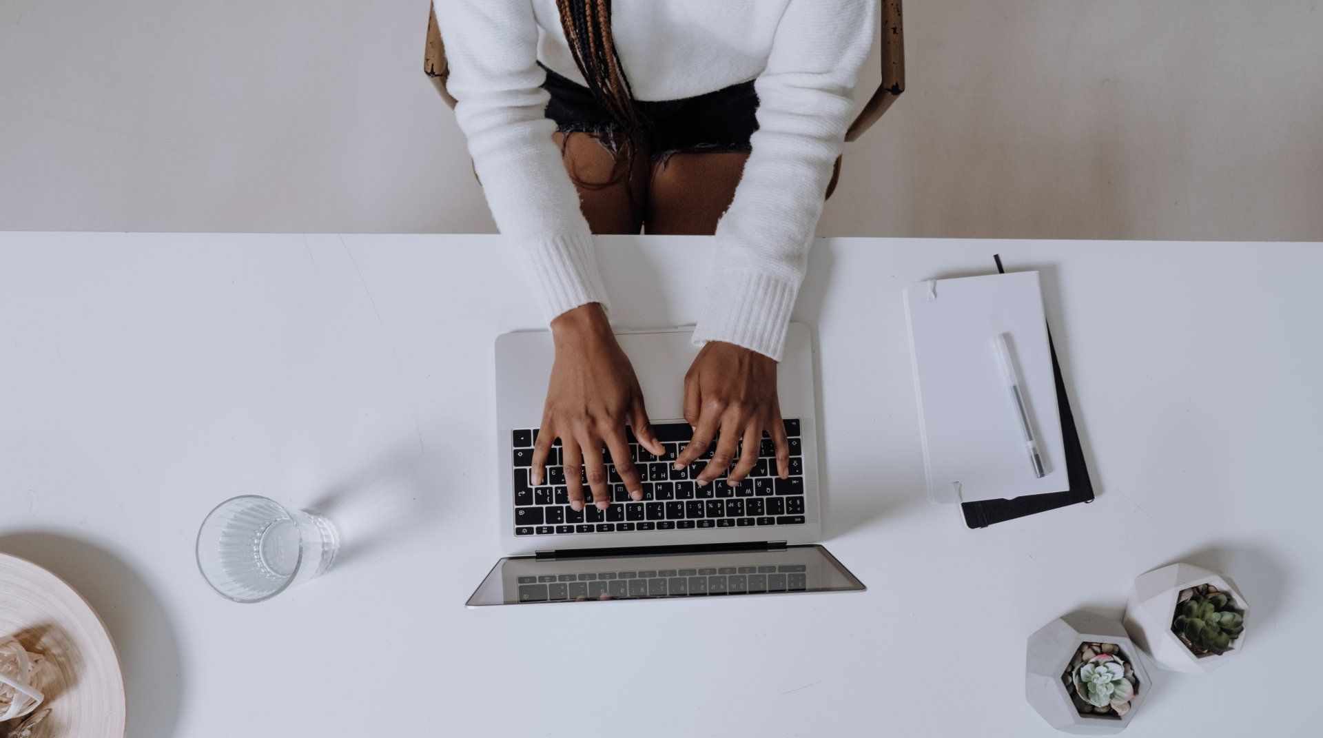 A woman is sitting at a desk typing on a laptop computer.