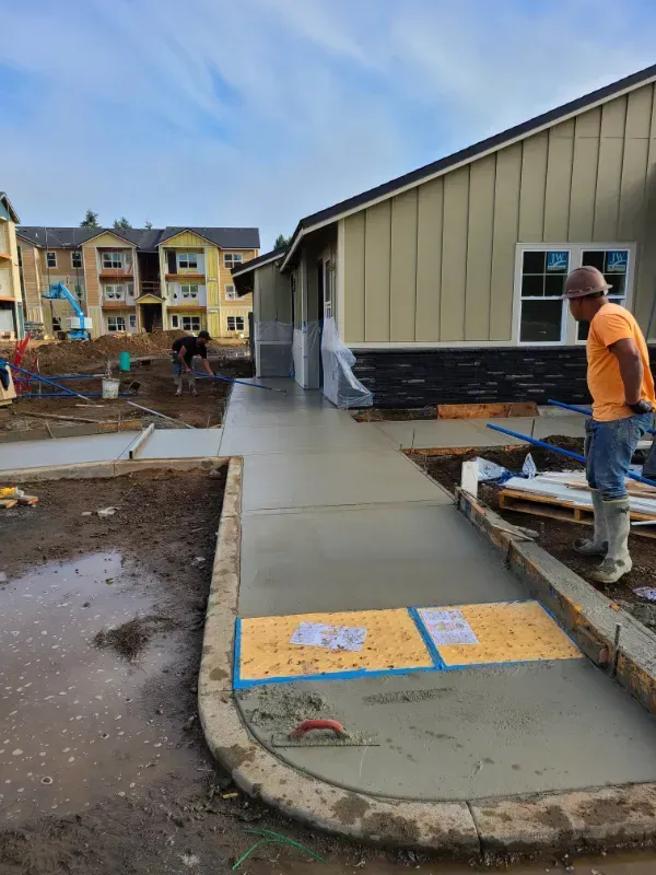 A man is standing on a sidewalk in front of a house under construction in Vancouver, WA by NAVA Concrete LLC
