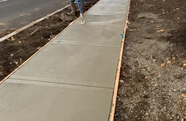 Freshly poured concrete sidewalk under construction beside bare dirt