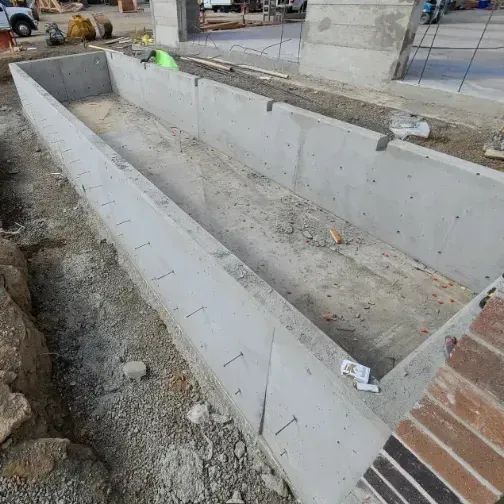 Concrete trench under construction. Long, rectangular structure with bare dirt inside, surrounded by concrete walls.