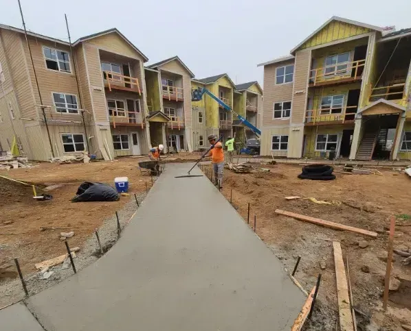 Construction site with fresh concrete walkway between apartment buildings and workers nearby