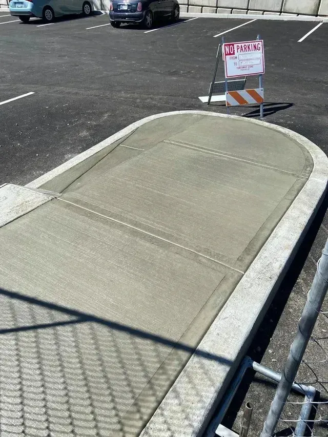 Concrete curb bordering a smooth sidewalk ramp near a paved parking area during installation.